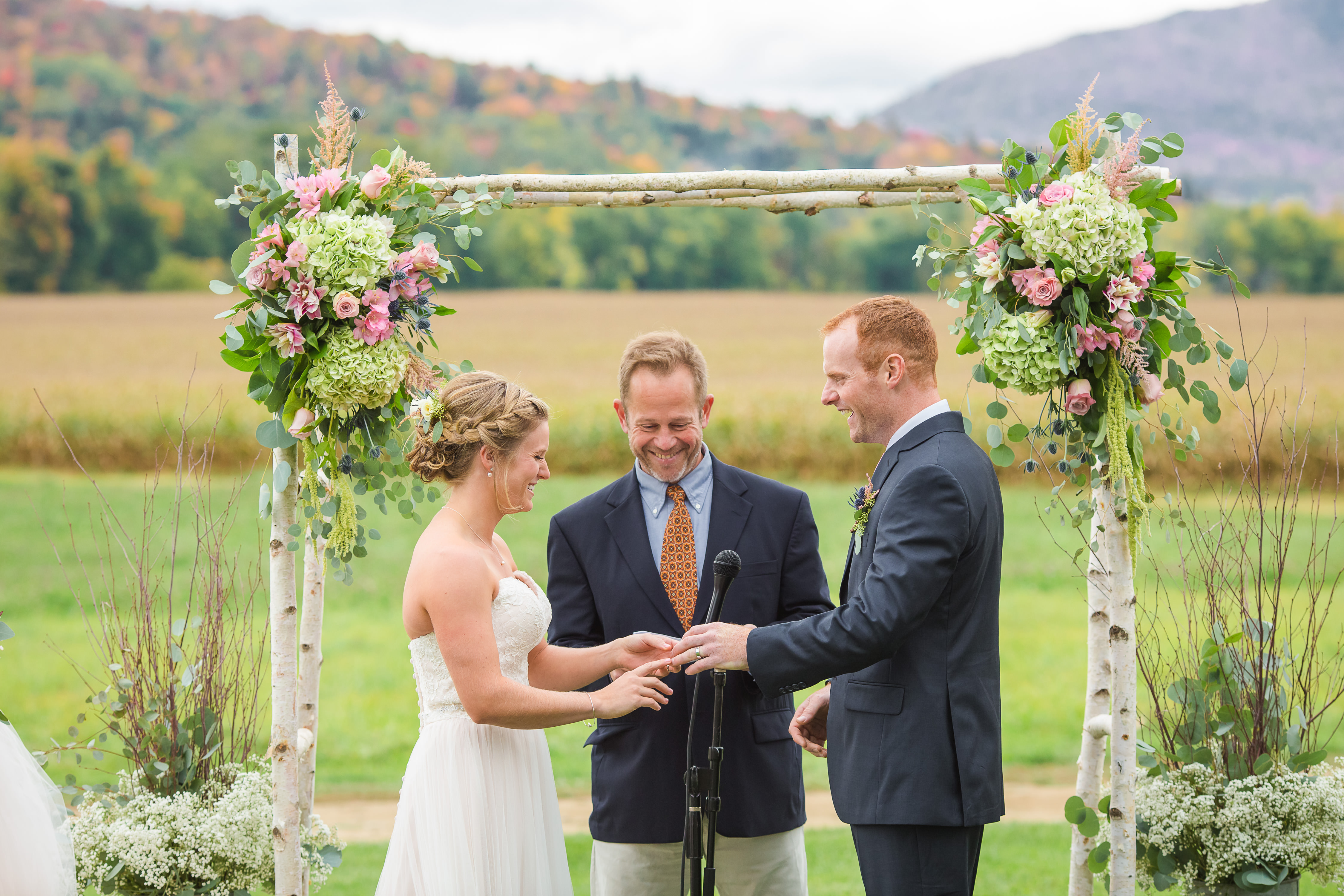 Bride, groom, and a wedding officiant standing under an outdoor wedding arch at a fall wedding in Vermont.